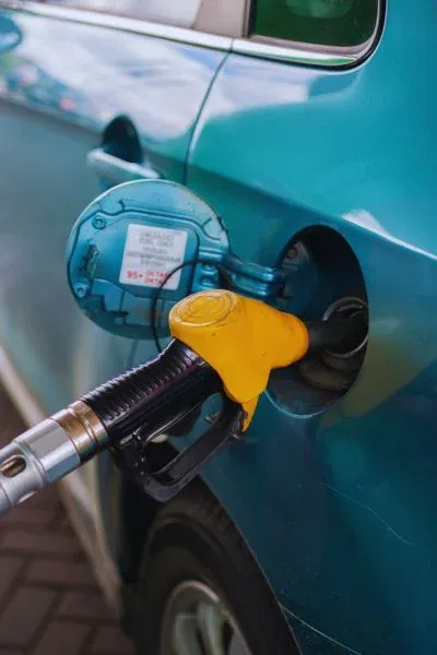 Pistolet de pompe à essence jaune engagé dans le réservoir d’une voiture bleue