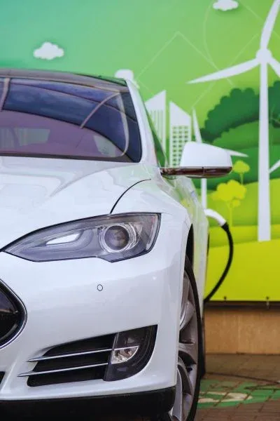 Voiture électrique blanche en recharge devant une fresque d’éoliennes et de ville verte